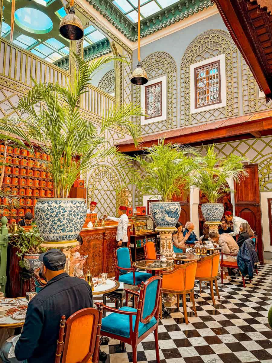 Inspiration photo: a tiled café atrium with palms, carved screens, and orange and blue chairs